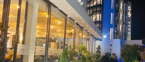 A modern building with a glass facade, a pathway leading to the entrance, and outdoor seating areas.