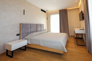 Habitación de hotel moderna con una cama grande, mesita de noche y un pequeño escritorio con silla.