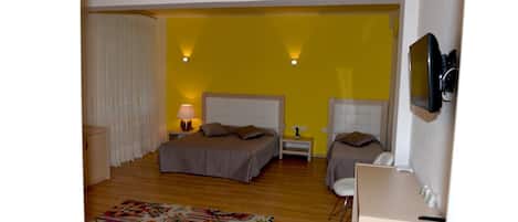 Un dormitorio con dos camas, una mesita de noche con lámpara, una alfombra colorida y un televisor fijado en la pared.
