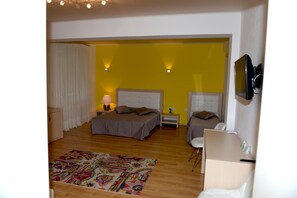 Een slaapkamer met twee bedden, een nachtkastje met een lamp, een kleurrijk vloerkleed en een aan de muur bevestigde televisie.