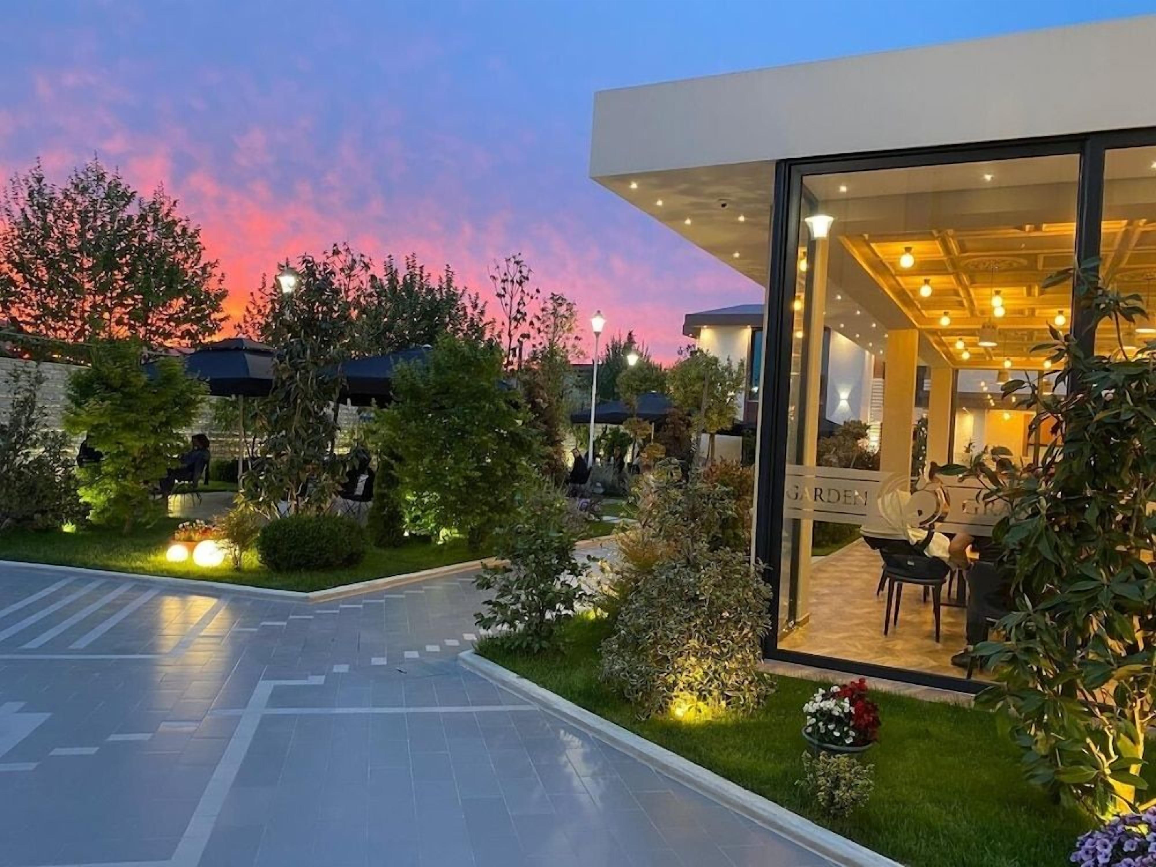 A modern building with a glass entrance, surrounded by well-maintained gardens and outdoor seating.