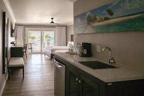 Habitación de hotel con cocina, una mesa de comedor y vista a la playa a través de la puerta corrediza de vidrio.