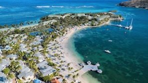 An aerial view of a coastal resort with multiple buildings, a beach, and clear blue waters. - St. Jamess Club Resort & Villas (Mamora Bay)