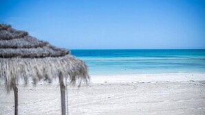 A beach with a thatched umbrella. - Club Calimera Yati Beach (Djerba Midun)