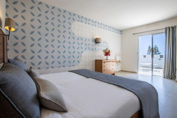A bedroom with a bed, a nightstand, a lamp, and a view of the outdoors. - Club Calimera Yati Beach (Djerba Midun)