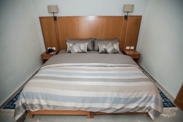 A bed with a wooden headboard, two bedside tables, and a striped bedspread. - Club Calimera Yati Beach (Djerba Midun)