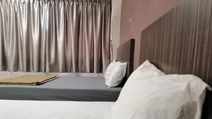 Ett hotellrum med en säng, en kudde, ett sängbord och en gardin.
