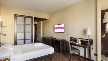 A hotel room with a bed, desk, chair, and a television displaying "STAY TUNED".