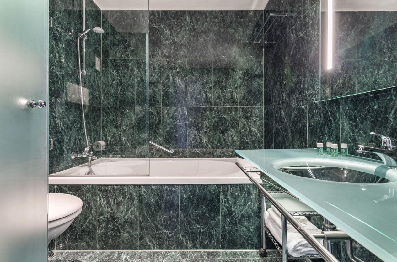 A modern bathroom with a marble wall, a glass-enclosed bathtub, and a glass sink.