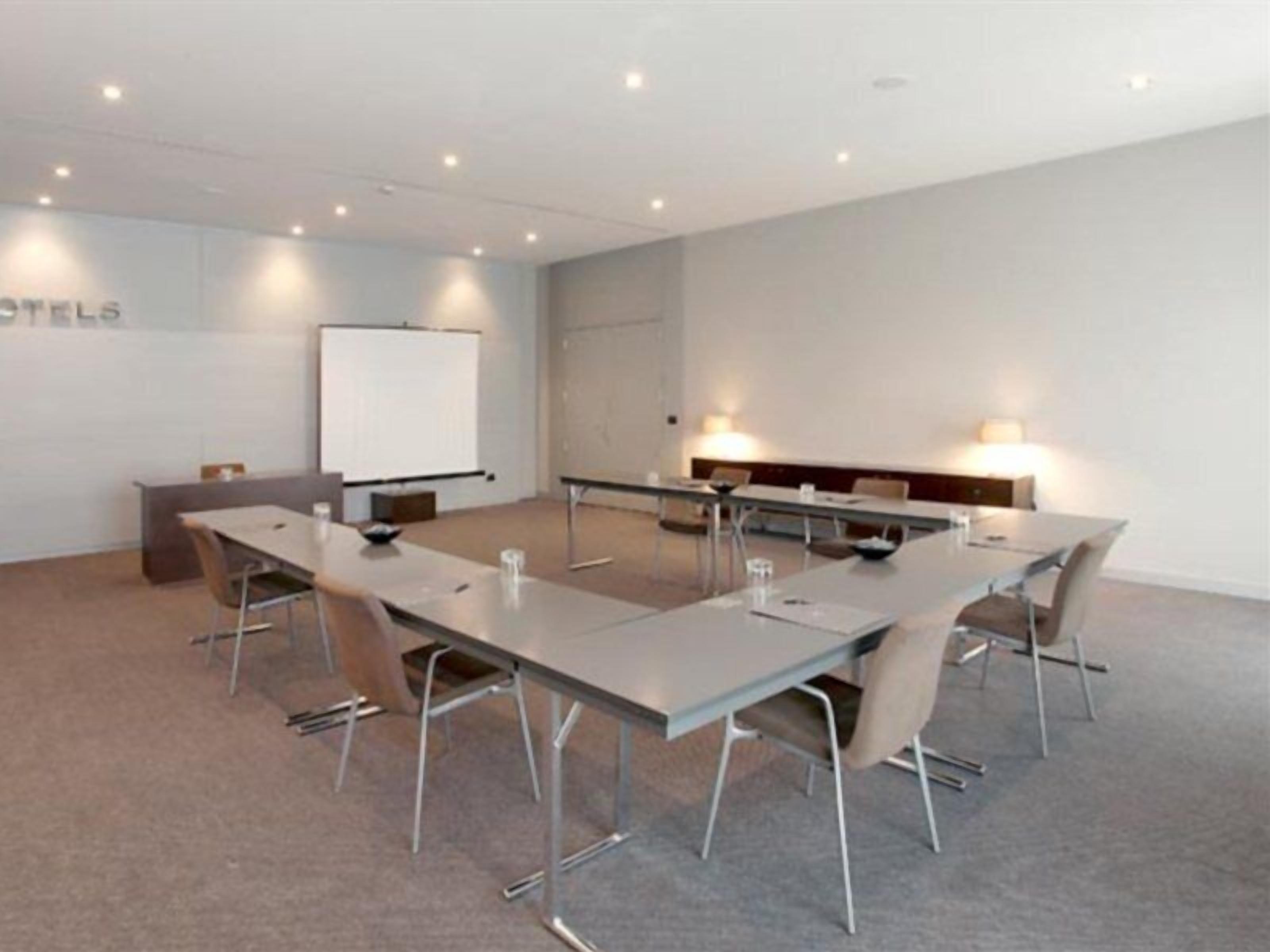 A conference room with a long table, chairs, a whiteboard, and a projector screen.