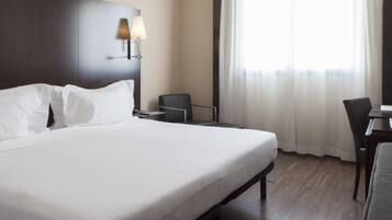 A hotel room with a large bed, a desk, a chair, and a lamp.