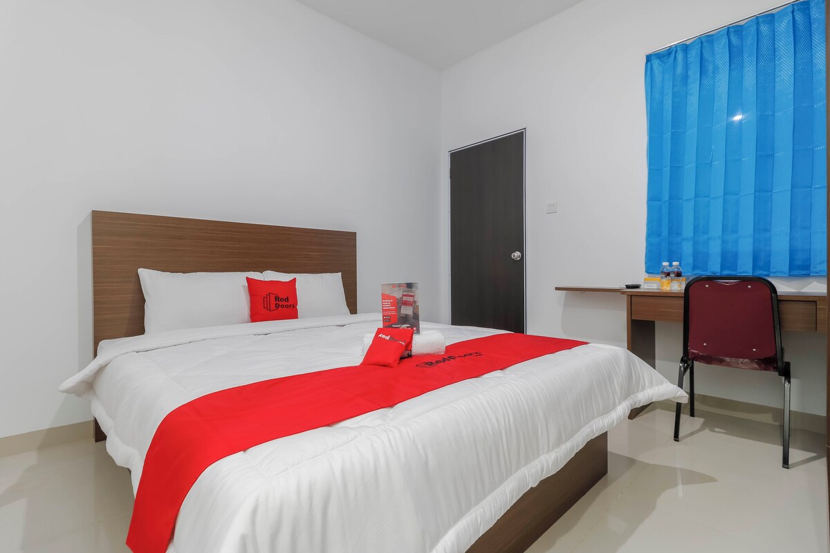 Habitación de hotel con cama, escritorio, silla, puerta y ventana con cortinas azules.