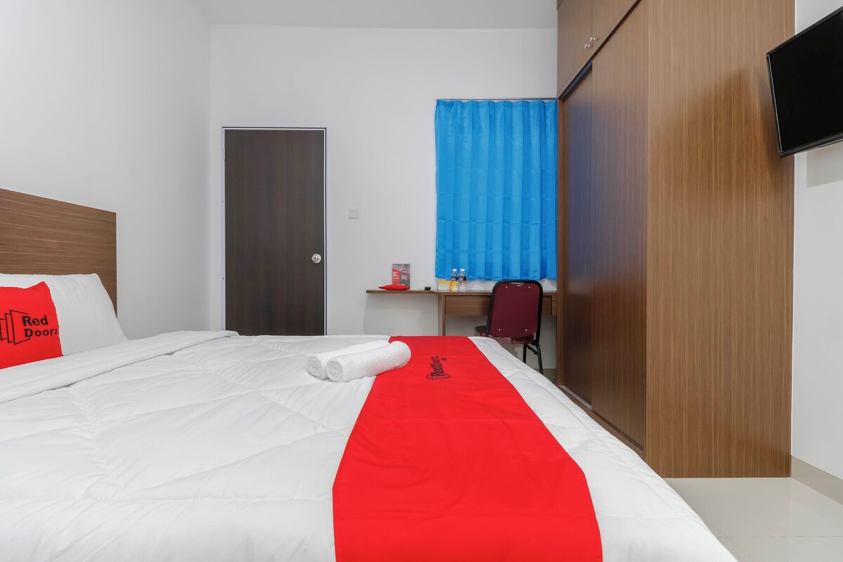 Habitación de hotel con una cama bien hecha, un escritorio con silla, armario y televisión en la pared.
