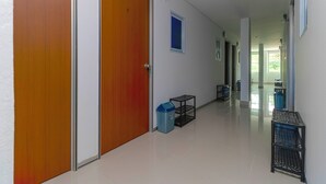 Un pasillo con puertas de madera, un cubo de basura, un estante pequeño y una ventana.