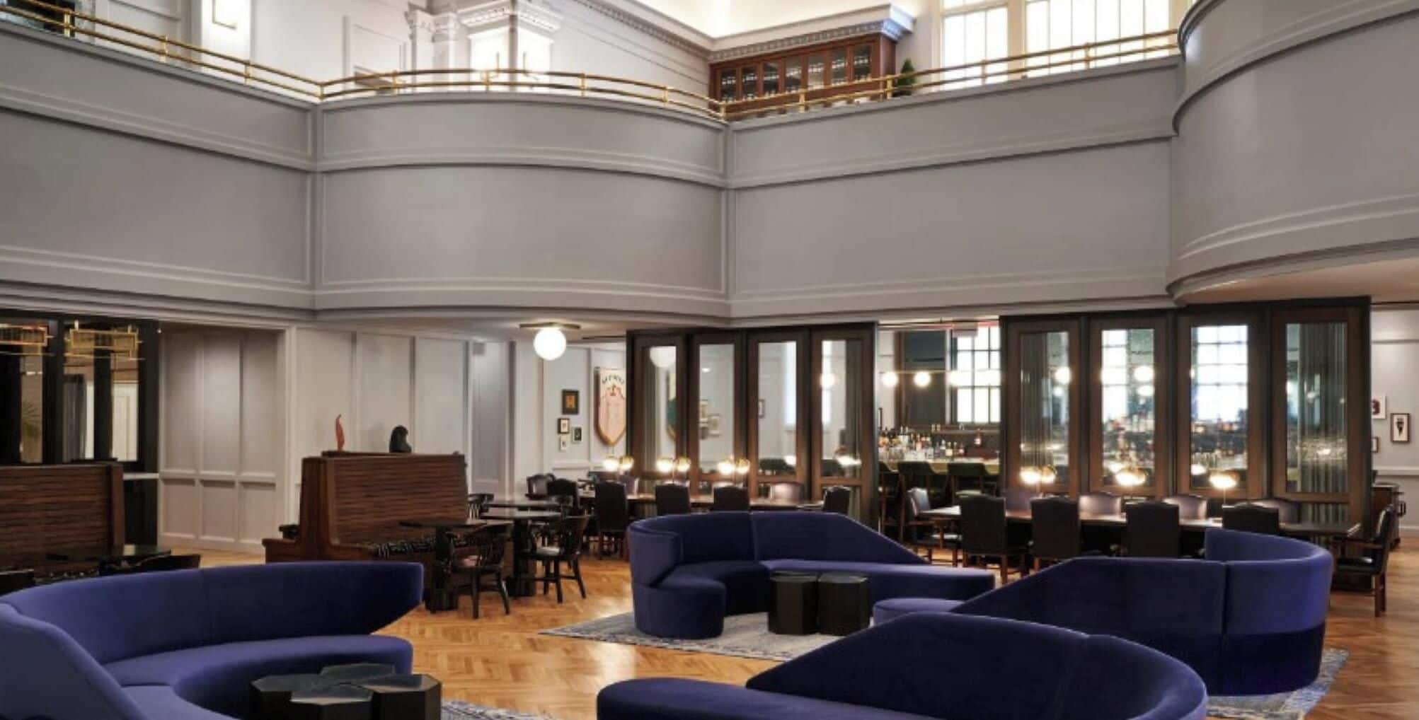 A spacious lobby with high ceilings, a central seating area with sofas, and a bar with multiple seating options.