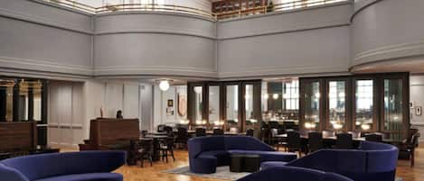 A spacious lobby with high ceilings, a central seating area with sofas, and a bar with multiple seating options.