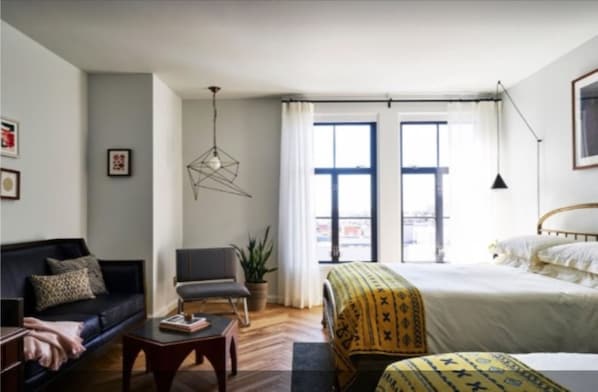 A modern bedroom with a bed, a sofa, a chair, a desk, and a hanging light fixture. - The Line DC (Washington)