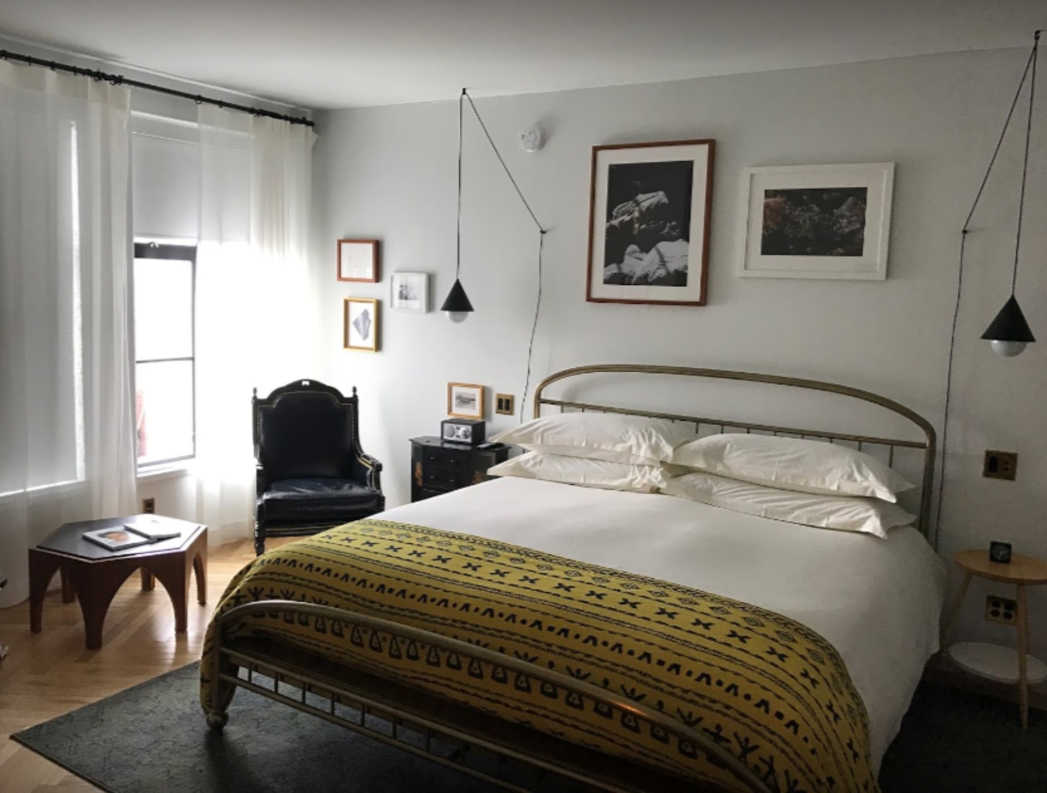 A bedroom with a bed, a chair, a small table, and a window with curtains.