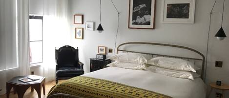 A bedroom with a bed, a chair, a small table, and a window with curtains.