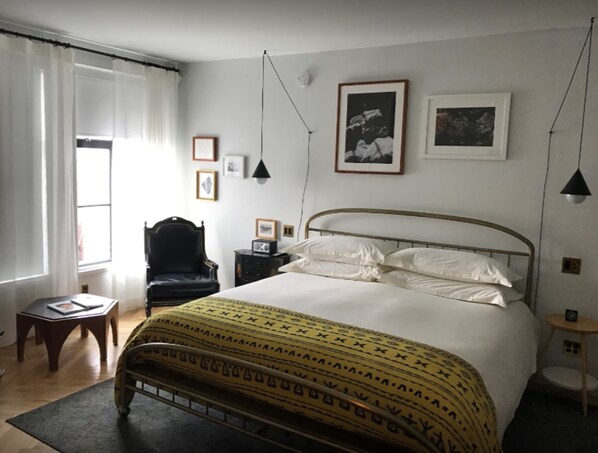 A bedroom with a bed, a chair, a small table, and a window with curtains. - The Line DC (Washington)