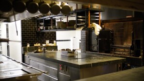 A commercial kitchen with stainless steel appliances, a brick wall, and hanging pots. - The Line DC (Washington)