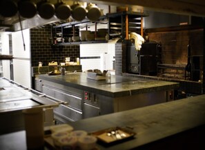 A commercial kitchen with stainless steel appliances, a brick wall, and hanging pots. - The Line DC (Washington)
