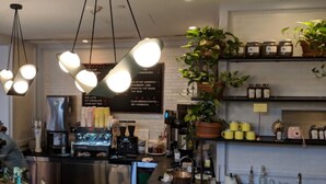 A coffee shop interior with hanging lights, a coffee machine, shelves with jars, and a menu board. - The Line DC (Washington)