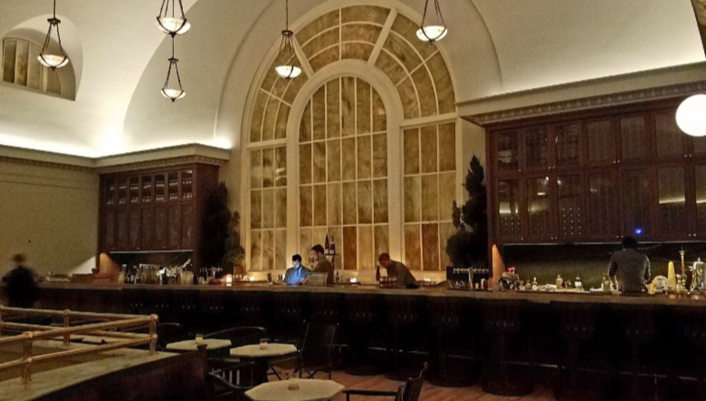 A bar area with a high arched window, hanging lights, and a counter with bar stools.