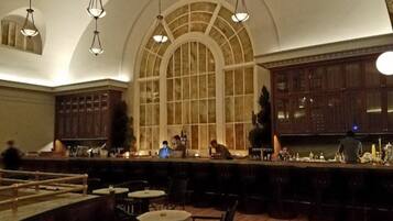 A bar area with a high arched window, hanging lights, and a counter with bar stools.