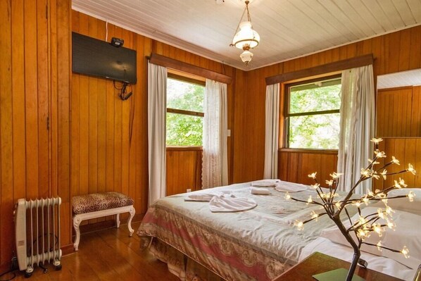 Una habitación con paneles de madera, una cama, un banco, un radiador y un televisor montado en la pared.