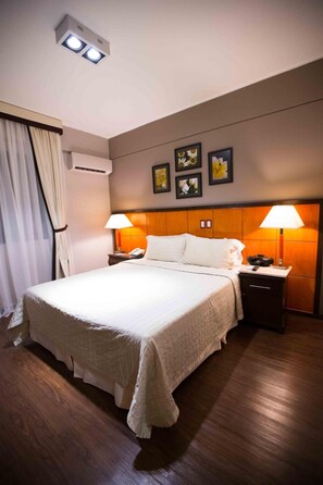 A hotel room with a large bed, bedside lamps, a wooden headboard, and a ceiling light fixture. - Las Ventanas Suites Hotel (Hernandarias)