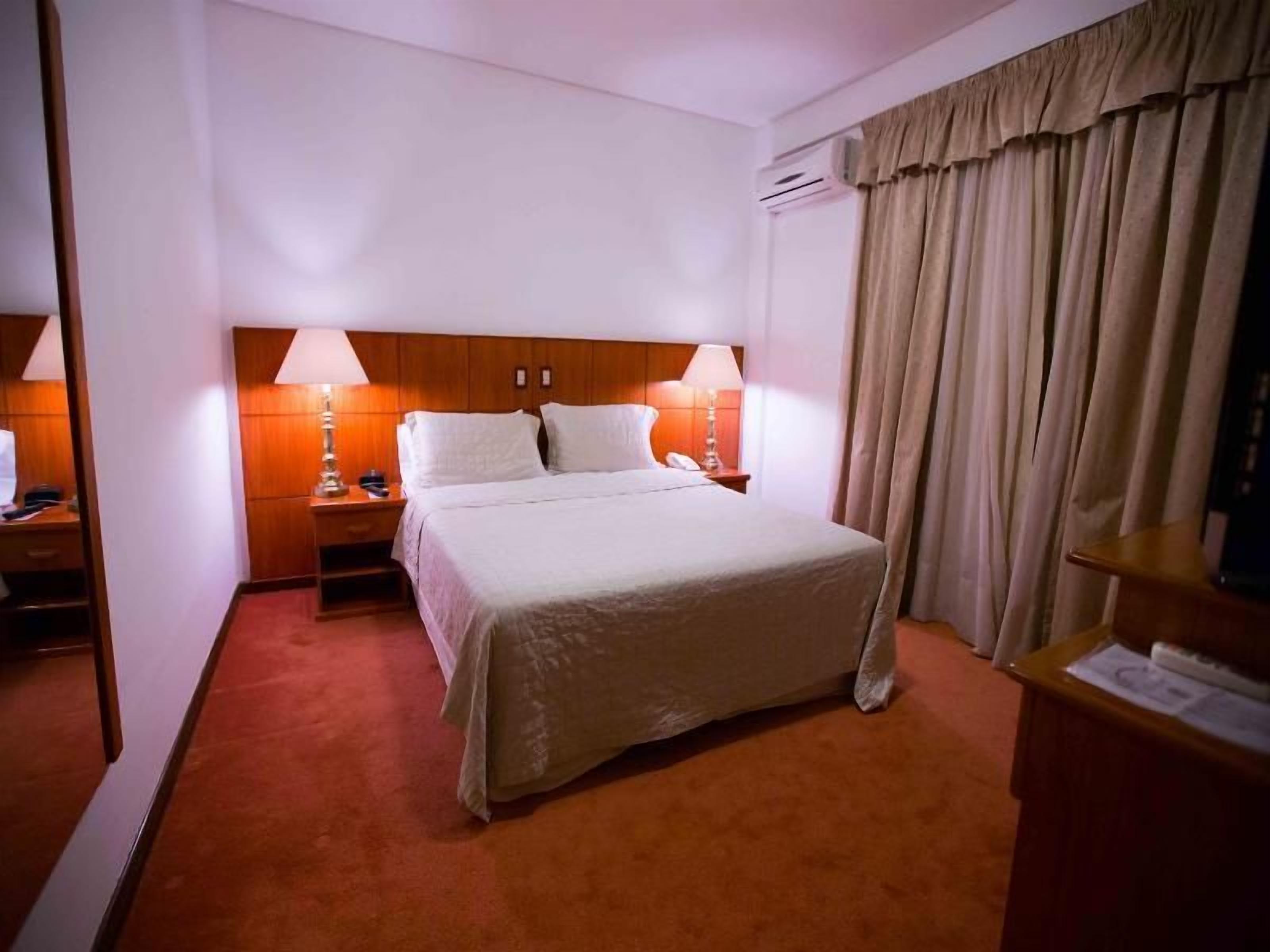 A hotel room with a bed, nightstands, lamps, a mirror, and a curtain.