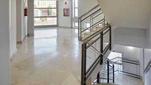 A spacious interior with a marble floor, a staircase with metal railings, and large windows allowing natural light.