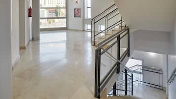 Un interior espacioso con suelo de mármol, una escalera con barandillas metálicas y ventanas amplias que dejan entrar luz natural.