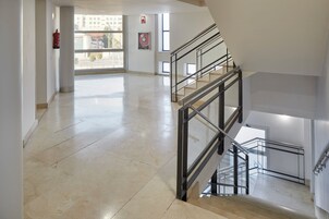 Un interior espacioso con suelo de mármol, una escalera con barandillas metálicas y ventanas amplias que dejan entrar luz natural.