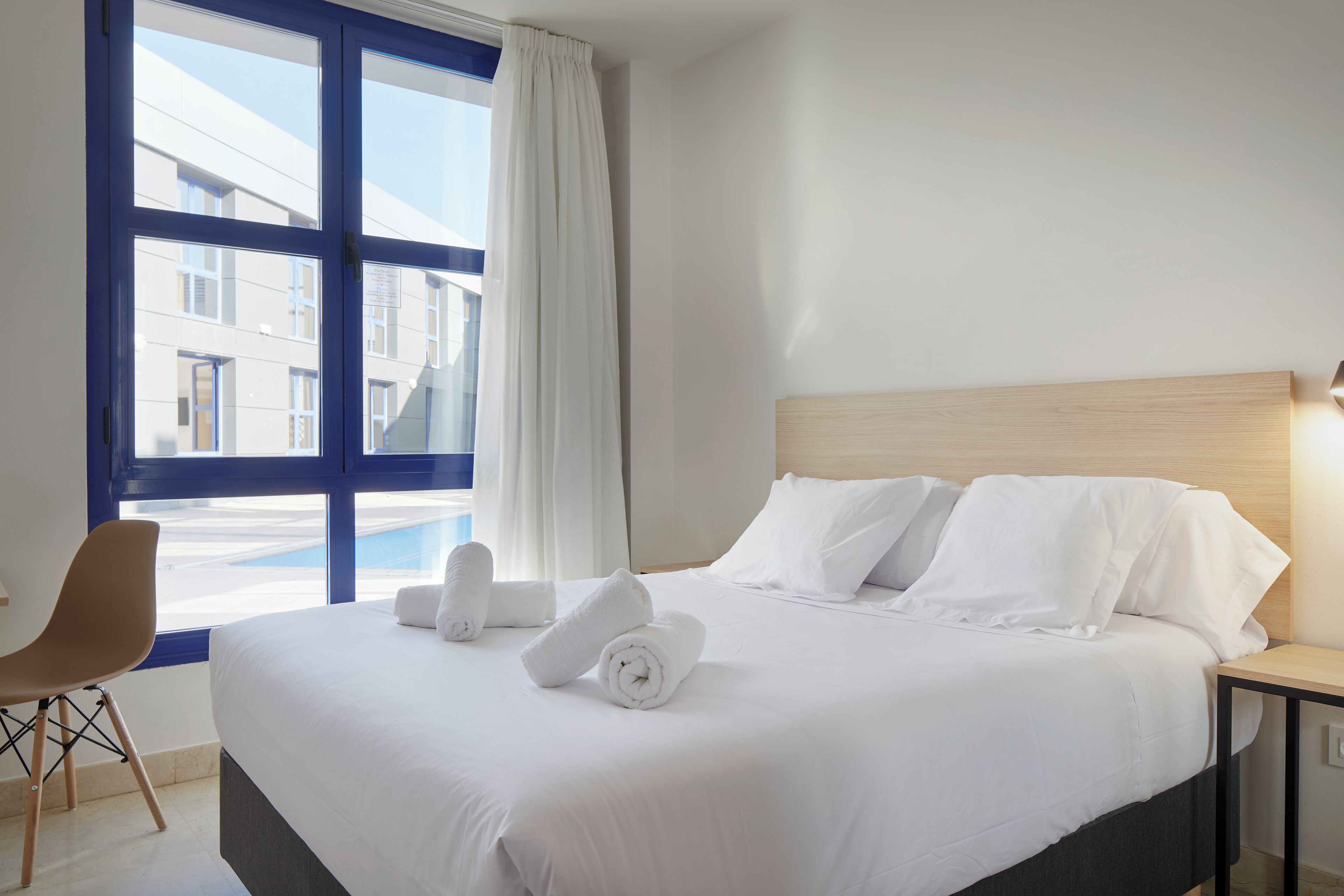Une chambre d’hôtel avec un grand lit, une chaise, une table de chevet et une fenêtre avec des rideaux.