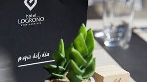 A small potted plant on a table with a wooden block and a black bag with the Hotel Logroño logo.