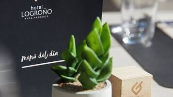 Una planta en maceta sobre una mesa, un bloque de madera con la marca del hotel y un bolso negro con la marca del hotel.