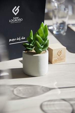 Une petite plante en pot est posée sur une table, à côté d’un bloc de bois et d’un sac noir orné du logo de l’hôtel Logroño.