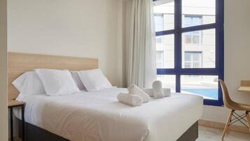 A hotel room with a bed, a desk, and a window with a view of buildings.