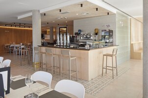 Zona de bar moderna con mostrador, taburetes y una máquina de café.