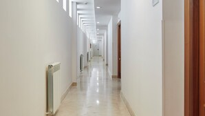 A long, narrow hallway with white walls, a tiled floor, and a series of doors on one side.