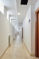 Un pasillo largo y estrecho con paredes blancas, suelo de baldosas y varios puertas a un lado.