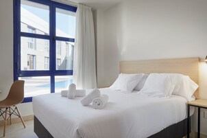 Habitación de hotel con una cama grande, una silla, una mesita de noche y una ventana con cortinas.
