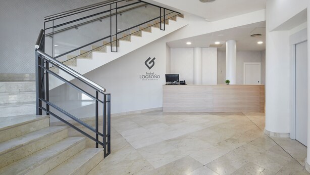 A hotel lobby with a staircase, a reception desk, and a logo on the wall.