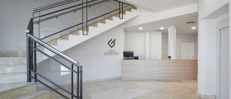 Vestíbulo de hotel con una escalera, una recepción y un logotipo en la pared.