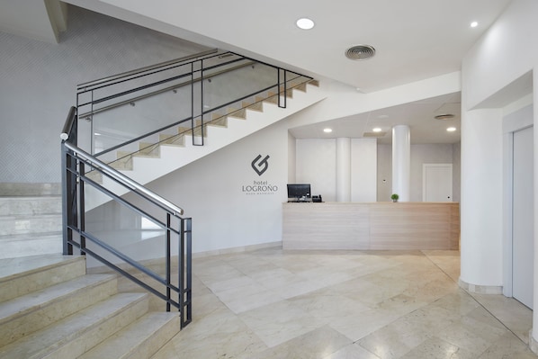 Un hall d’hôtel avec un escalier, un comptoir d’accueil et un logo sur le mur.