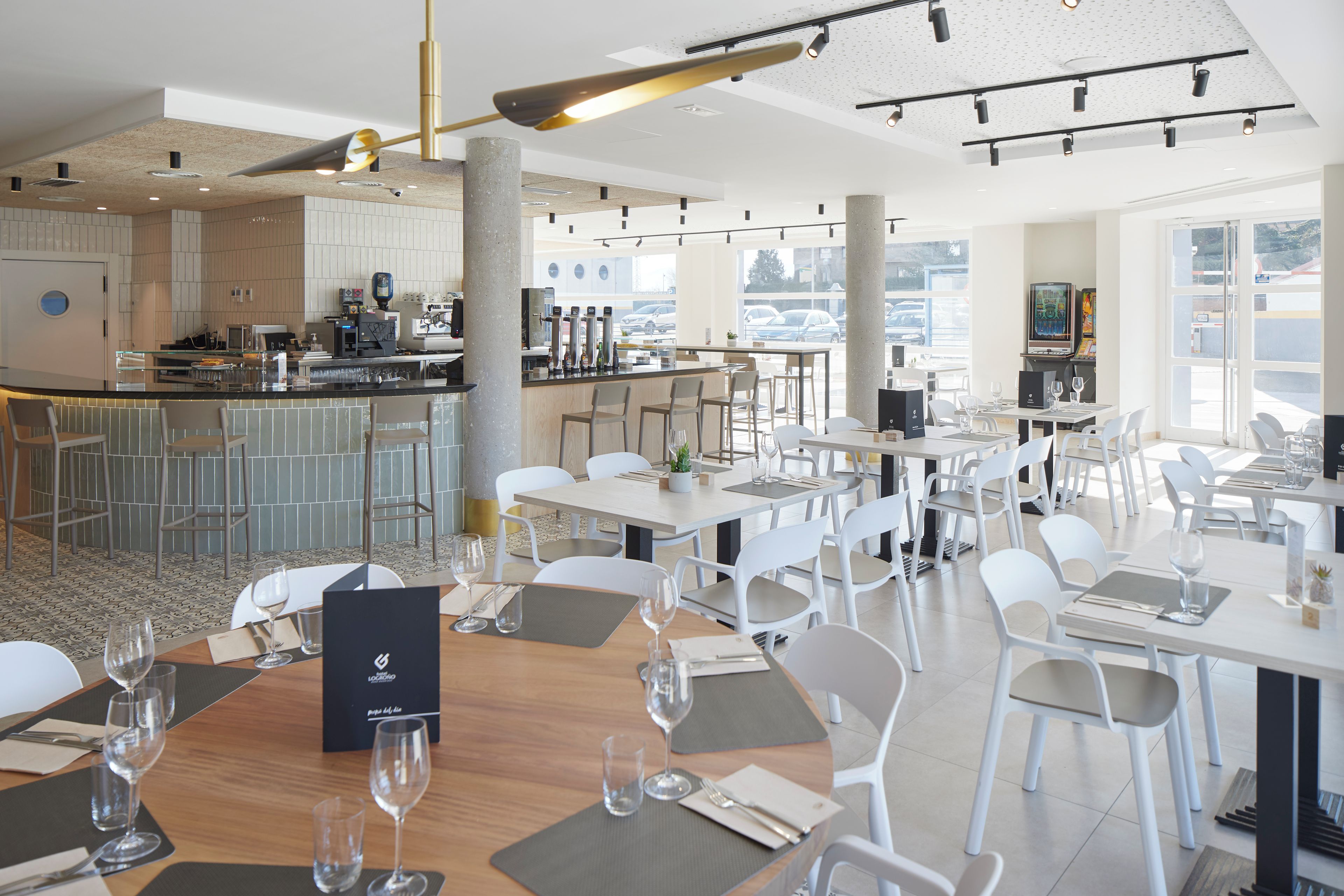 Un restaurante moderno con zona de bar, sillas y mesas blancas preparadas para comer.