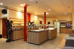 A hotel lobby with a reception desk, a statue, and a coffee station. - Hotel Konigshof Am Funkturm (Hannover)