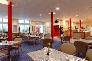 Uma sala de jantar de hotel com mesas, cadeiras e um balcão.